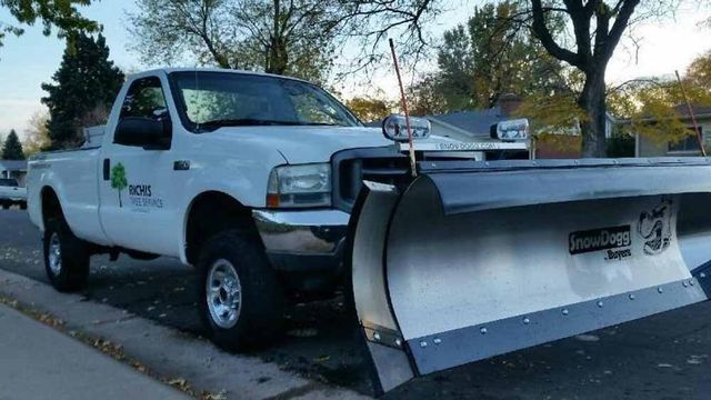A white truck with a snow plow attached to it is parked on the side of the road.